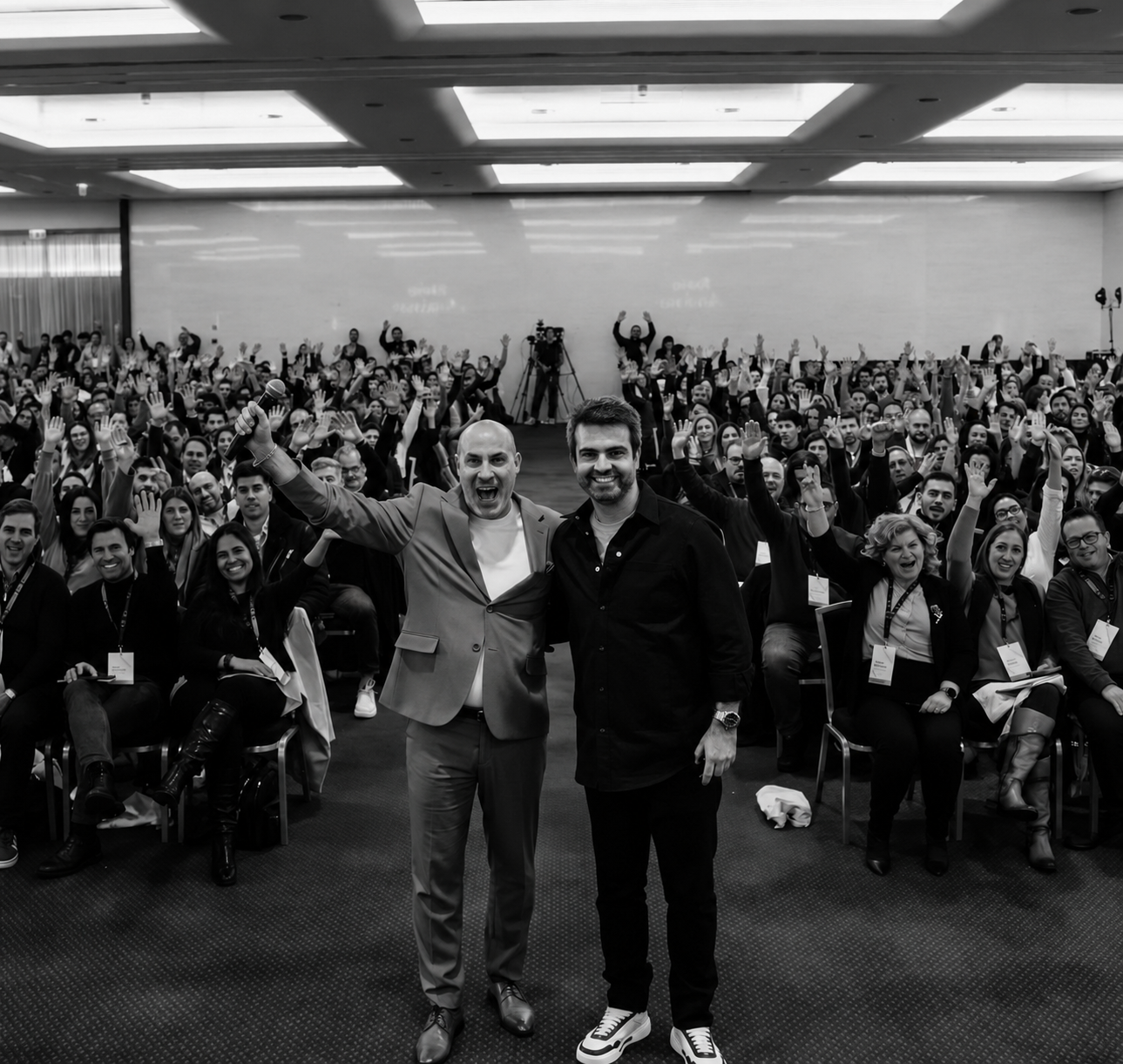 Flávio on stage with a co-host, audience cheering with raised arms.